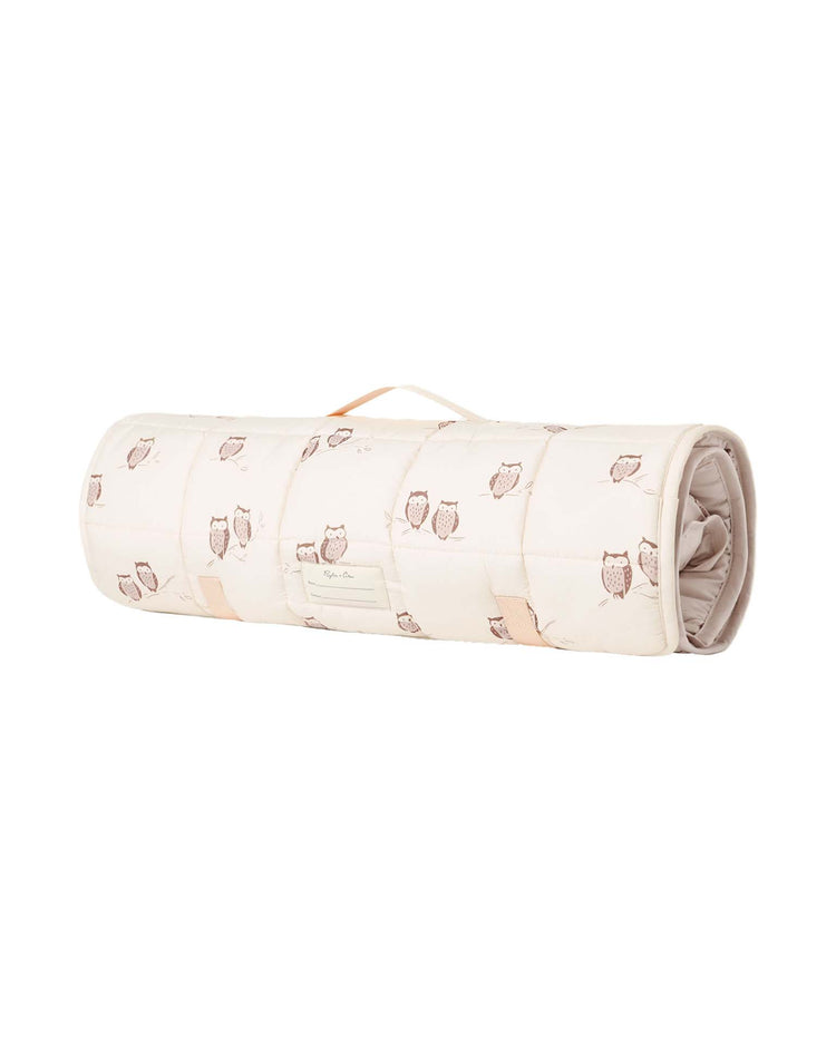 The rylee + cru nap mat in owls is a rolled-up, quilted nap mat with a convenient carrying handle. It features a charming pattern of small brown owls on a cream background, includes a soft micro-fleece blanket for extra coziness, and comes with a removable pillow for added comfort.