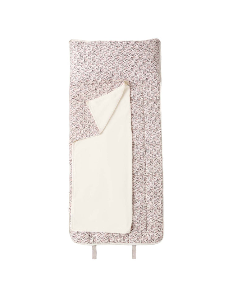 A folded rylee + cru nap mat in primrose, featuring a cream-colored micro-fleece blanket partially draped over it and a removable pillow, displayed on a white background.