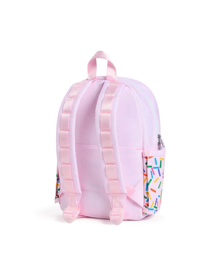 The State Bags Kane Mini Backpack in Sprinkles is a small pink backpack with light pink straps, a pastel zipper, and side pockets decorated with a colorful sprinkles pattern, displayed from the back against a white background.