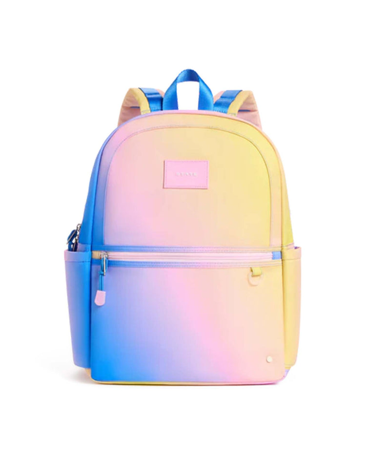 The STATE Bags Kane Backpack in a blue, pink, and yellow gradient features a pastel ombre design, front zippered pocket, side pockets, and light blue straps.