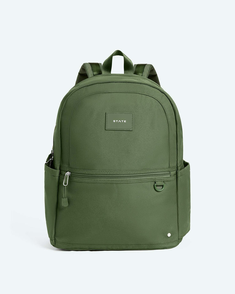 The Kane Large Double Pocket Backpack in Olive by STATE Bags features a front zip pocket, two side pockets, and a small rectangular STATE patch on the front. This stylish school backpack is displayed against a light gray background.