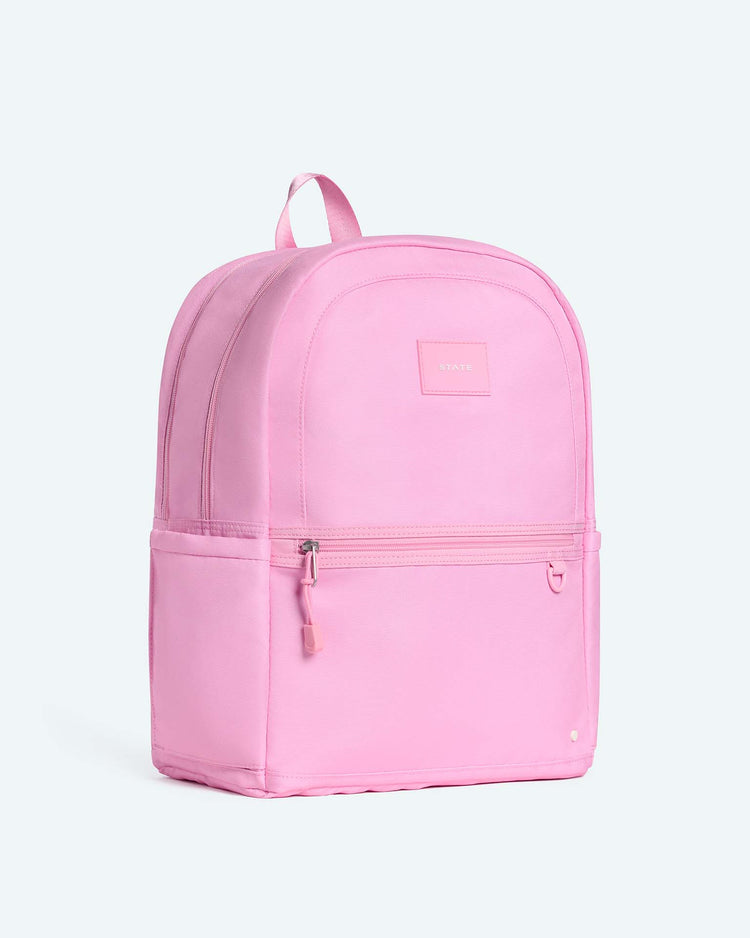 The Kane Large Double Pocket Backpack in Pink by State Bags stands upright against a light background. Featuring dual front zippered pockets, a small stitched brand label, and a top handle, it’s the perfect stylish backpack for school.