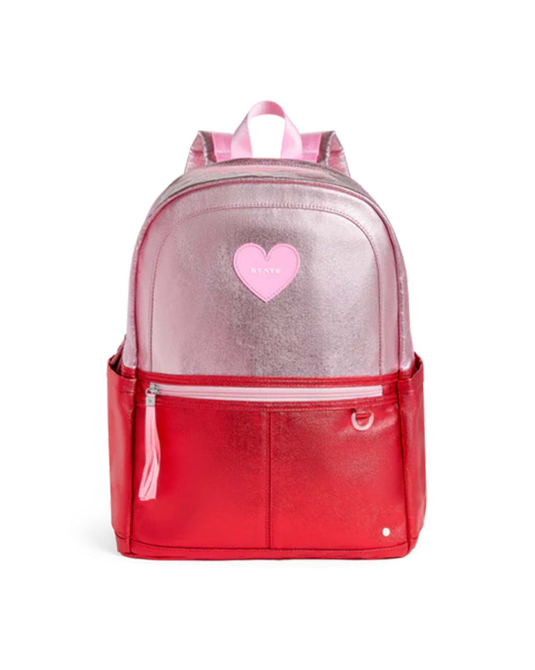 The Kane Double Pocket Backpack in pink + red colorblock by State Bags features a shiny metallic pink top half, a vibrant red bottom half, two convenient side pockets, and a playful pink heart patch on the front.