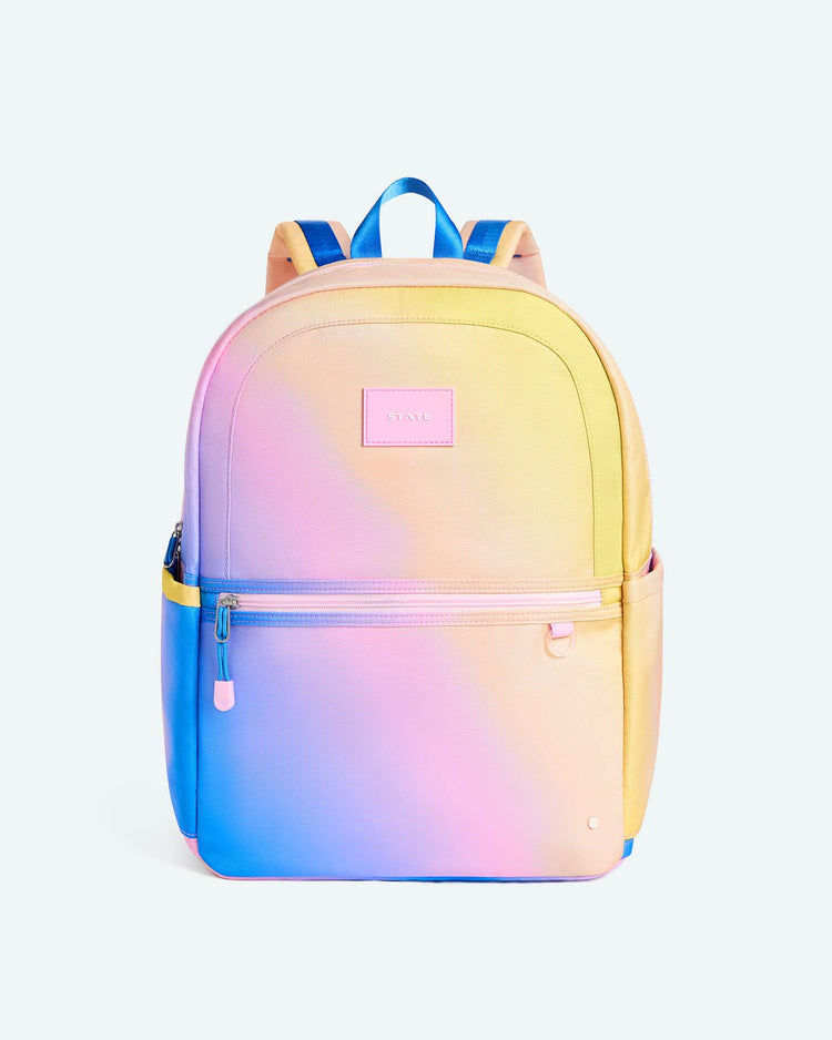 The State Bags Kane Large Double Pocket Backpack in a blue, pink, and yellow gradient features a pastel design with two front zipper pockets, two side pockets, and is ideal for everyday school use.