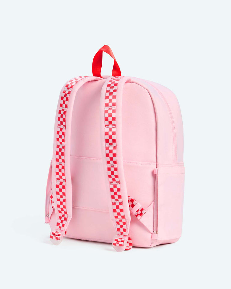 A light pink Kane Backpack in Cherry from State Bags, featuring red and white checkered straps and a red handle, is displayed against a plain light background.