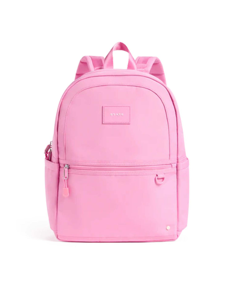 The Kane Backpack in Pink by State Bags features a vibrant pink design, a convenient front zipper pocket, side pockets, and a top handle. The State Bags brand label is displayed on the front.