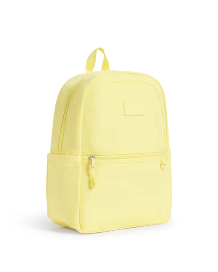The Kane Backpack in Butter Yellow by STATE Bags is pictured against a plain white background, featuring a front zip pocket, side pocket, and a top handle—making it a stylish choice for school or travel.