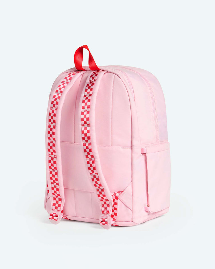 A Kane Double Pocket Backpack in Cherry from STATE Bags, featuring red and white checkerboard straps, a red handle, side pockets, and a light pink hue, is positioned upright against a plain light background—the perfect school backpack for any style-conscious student.