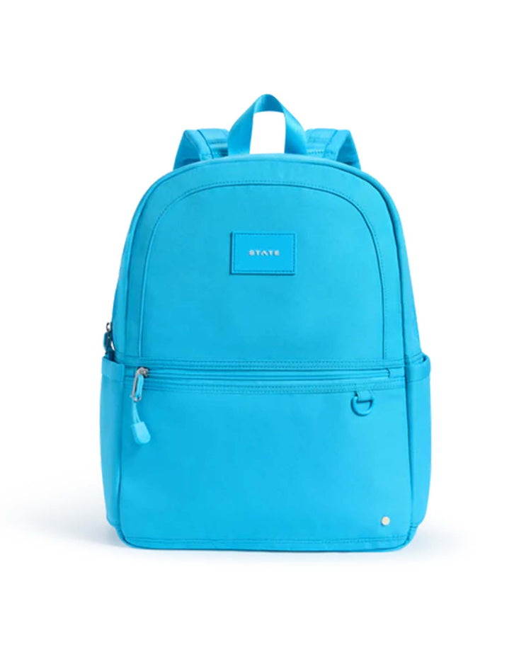 The Kane Backpack in bright blue from State Bags features a front zipper pocket, convenient side pockets, top handles, and a small State Bags label centered on the front. Its simple, modern design with minimal detailing makes it ideal for school or everyday adventures.