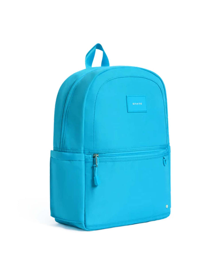 The Kane Backpack in bright blue from State Bags features a top handle, front zipper pocket, and side pocket, photographed against a plain white background. The main compartment is closed and the small State Bags brand label is visible on the front—making it an ideal everyday school backpack.