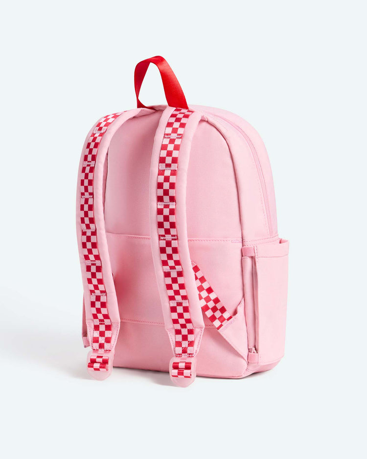 A State Bags Kane Mini Backpack in Cherry, featuring pink fabric, red-and-white checkered shoulder straps, and a red carrying handle, displayed from the back against a light background. The perfect kids backpack for everyday adventures.