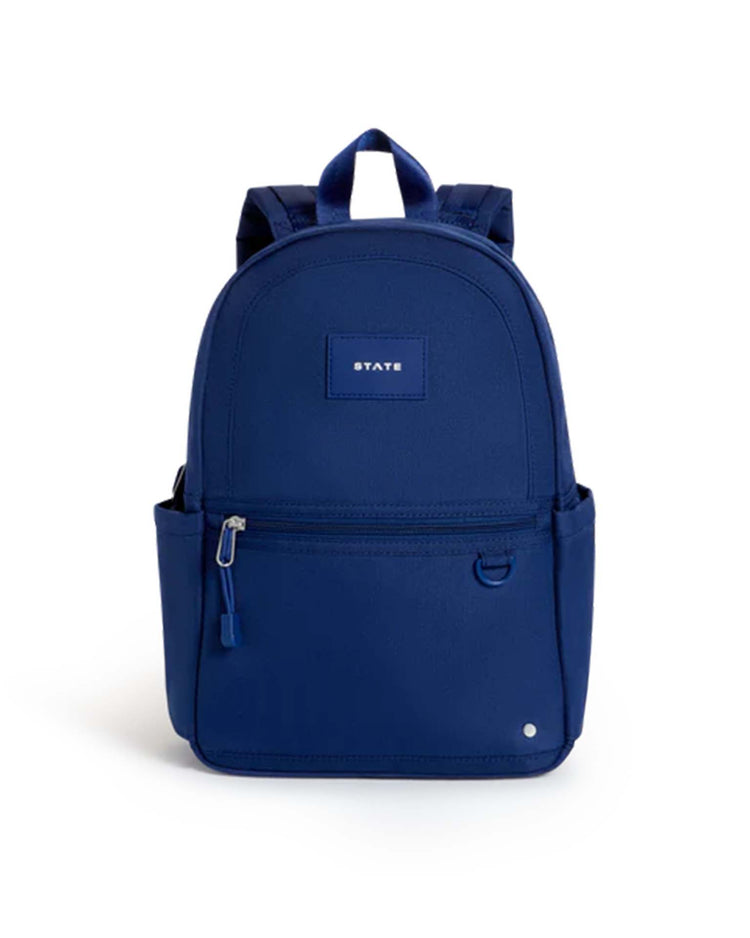 A navy Kane Mini Backpack by STATE Bags featuring a front zipper pocket, side pockets, padded shoulder straps, and a small rectangular label on the front that reads "STATE." Ideal for toddlers or as a mini backpack, this bag is shown against a white background.