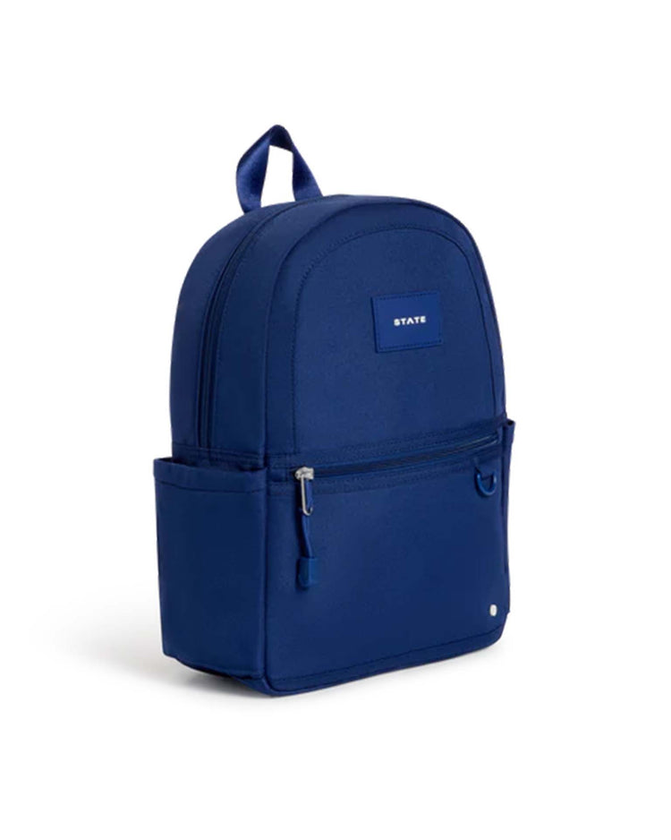 A navy kane mini backpack by STATE Bags featuring a front zipper pocket, two side pockets, a carrying loop on top, and a small rectangular label that says “STATE.”.