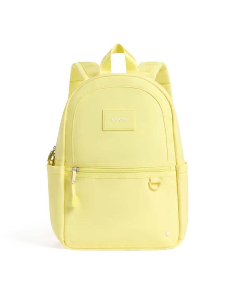 A butter yellow Kane Mini backpack from STATE Bags, featuring two front zippered pockets, side pockets, and a top handle. Designed as the perfect toddler backpack, it boasts padded shoulder straps and a small rectangular label on the front.