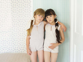 Two young girls in matching outfits standing against a light-colored wall.