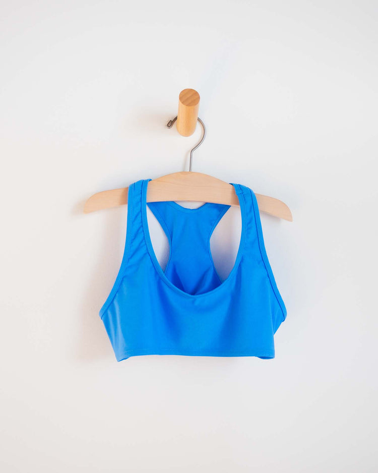 A vibrant "luisa two-piece swimsuit in mare" by sunchild, ideal for kids’ swimwear, hangs on a wooden hanger hooked onto a peg against a white wall.