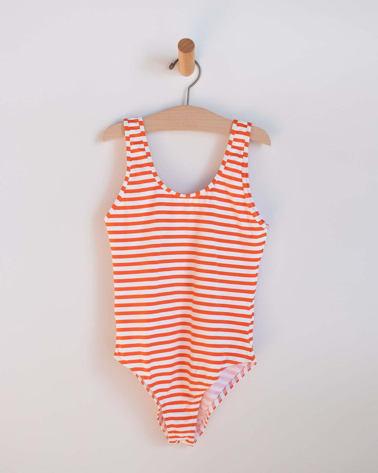 The lou one-piece swimsuit in soda by sunchild, featuring red and white stripes, hangs on a wooden hanger against a white wall—a timeless summer essential.