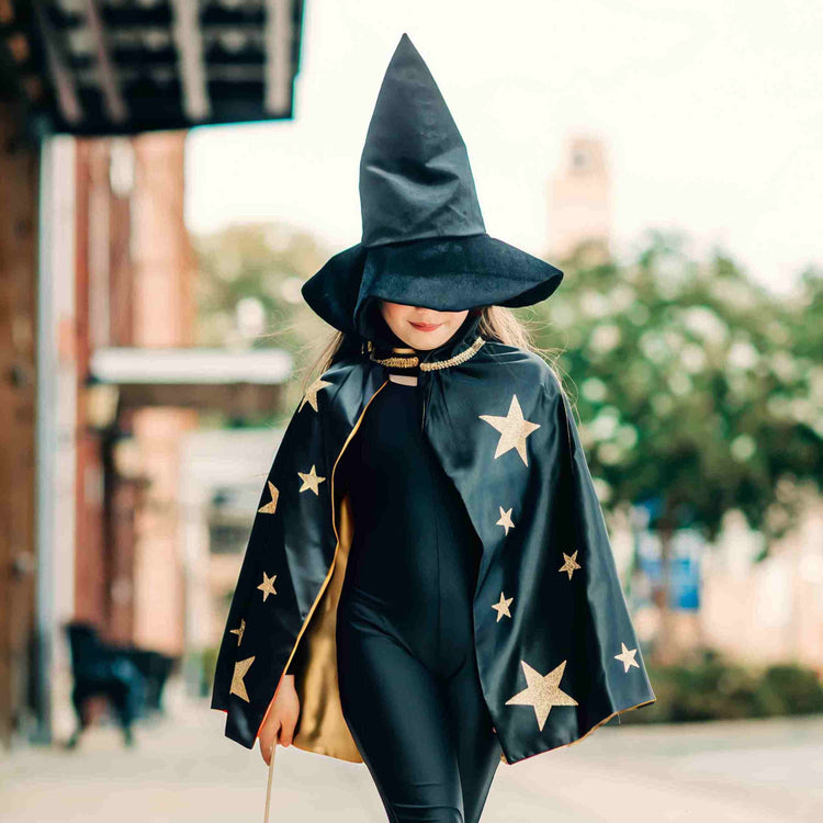A child wearing the Bailey and Ava Spellbound Witch Costume Set in Black, complete with a glitter star cape and velvet witch hat, walks outside, capturing the magic of the moment.