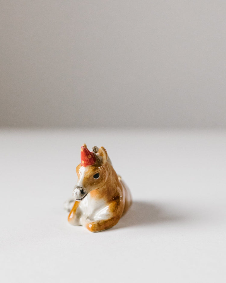 A small, ceramic Camp Hollow Year of the Horse Cake Topper with painted details, positioned against a plain, light grey background.