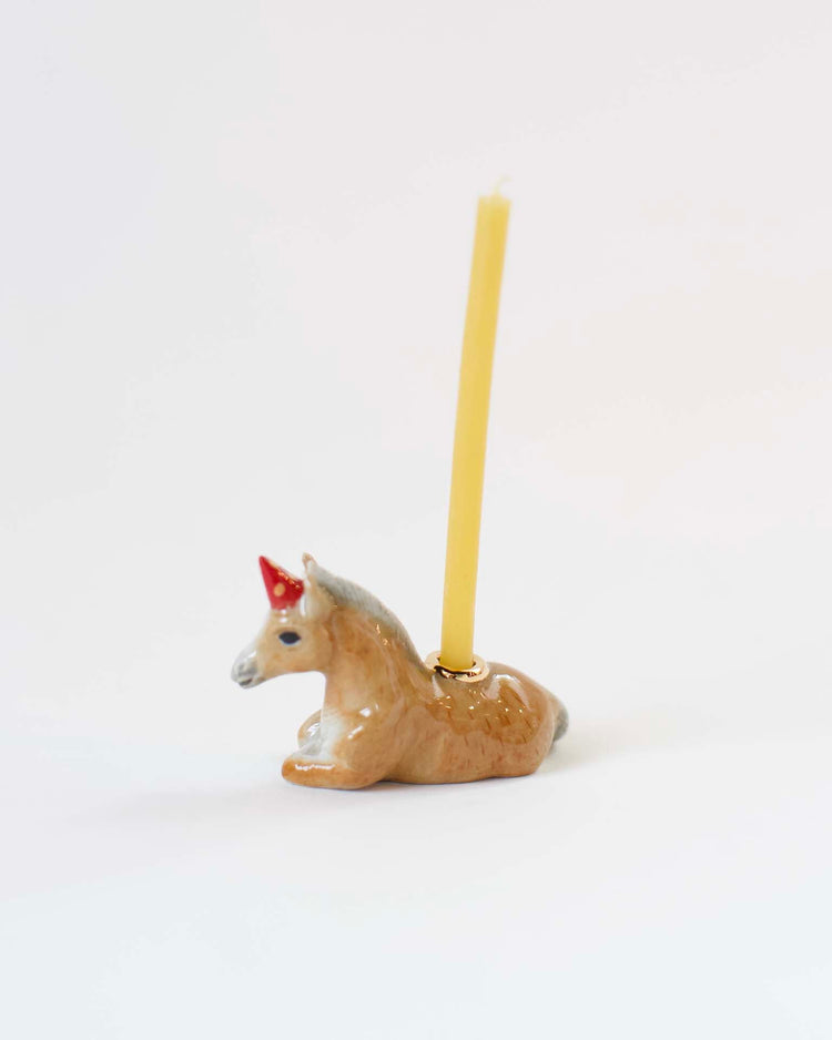 A hand-painted ceramic camp hollow unicorn candle holder with a yellow candle on a white background.