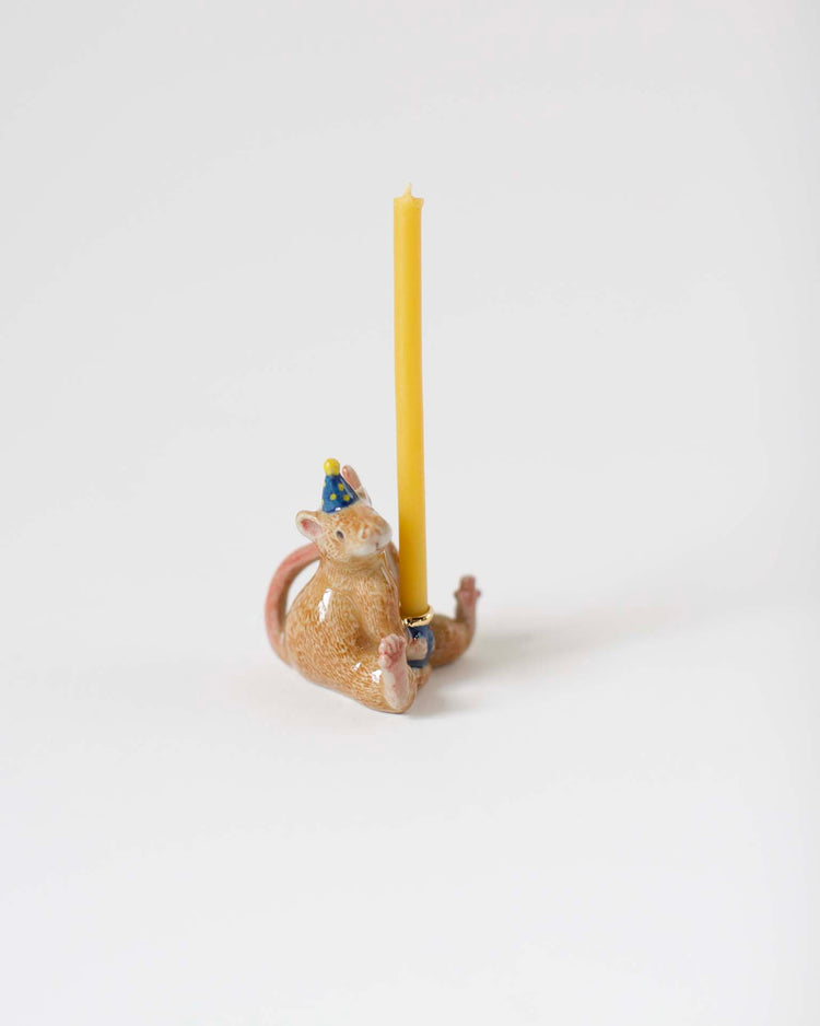Ceramic figurine of a smiling cat dressed in a party hat holding a yellow candle, set against a plain white background, hand-painted with Camp Hollow's "Year of the Rat" cake topper.