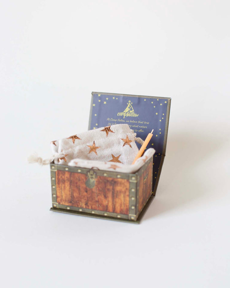 A small decorative ceramic chest with an open lid, containing a white pouch with golden stars and two colored pencils, against a plain background.