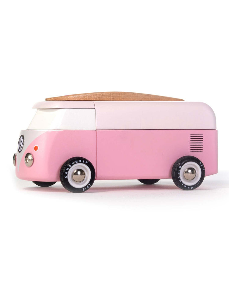 The candylab VW beach bus pink is a charming pink and white wooden surf van with black wheels and a wooden roof, inspired by the classic Volkswagen camper—perfect for imaginative play. Shown on a white background.