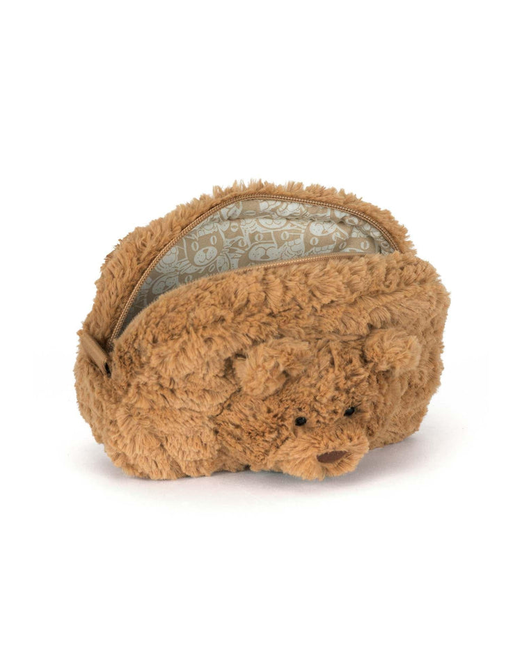 The Jellycat Bartholomew Bear Pouch is a small, brown pouch shaped like Bartholomew Bear’s face, with a zipper opening and patterned lining inside.