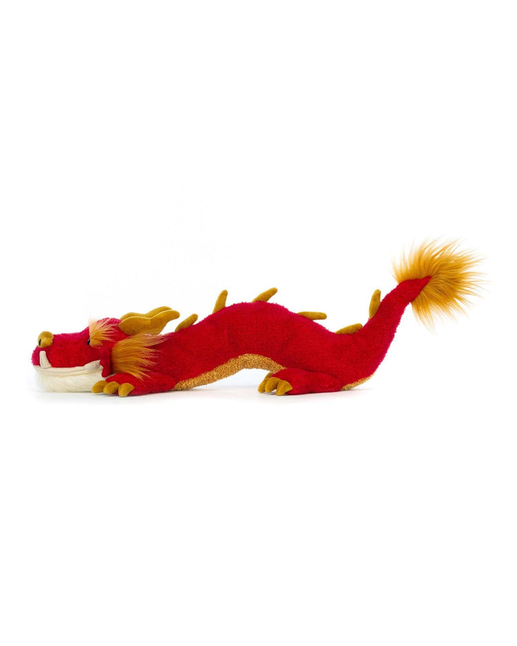 A Jellycat Festival Dragon toy featuring gold accents, a long body, and an orange-tipped tail, positioned horizontally.