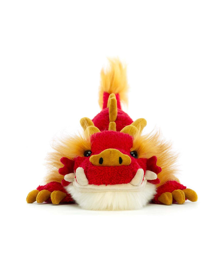A Jellycat Festival Dragon with yellow accents and a fluffy mane, lying flat on a white background. Perfect for any celebration, this delightful stuffed animal brings a festive touch to any space.