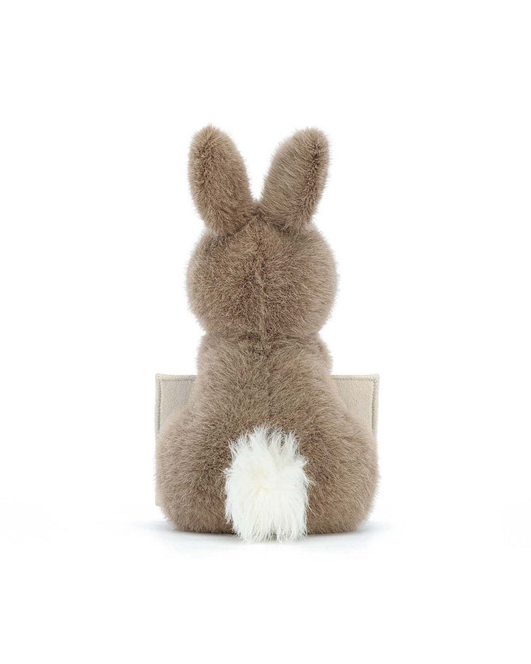 Back view of a fluffy brown "Messenger Bunny" stuffed toy from Jellycat, featuring a white tail, sitting upright on a plain white background. A perfect stuffed animal to cuddle or share a personal message with.