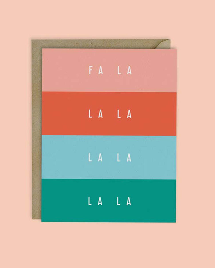 The "fa la la colorblock christmas card" by mellowworks is a vibrant design showcasing bands of pink, red, blue, and teal with the word "LA" repeated. It includes a kraft paper envelope and offers a blank interior for your personal message.