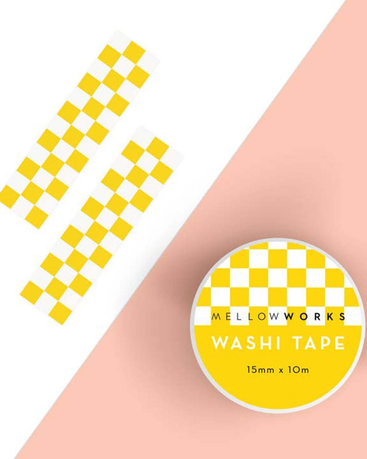 A roll of mellowworks yellow checkerboard washi tape is placed beside two strips of the same tape on a two-toned white and peach background, perfect for those looking to decorate cards or create charming gift tags.