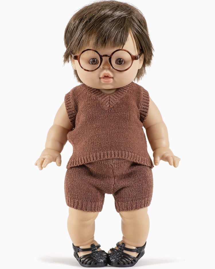 A small Minikane doll with brown hair, wearing round glasses, a léonardo knit tank in heather caramel, matching shorts, and black shoes stands upright.