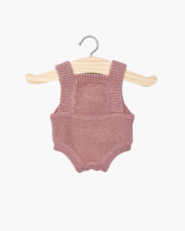 Tea pink lou knit romper featuring shoulder straps, showcased on a wooden hanger against a white background. Perfectly suited for Minikane dolls, it adds a touch of charm to any collection.