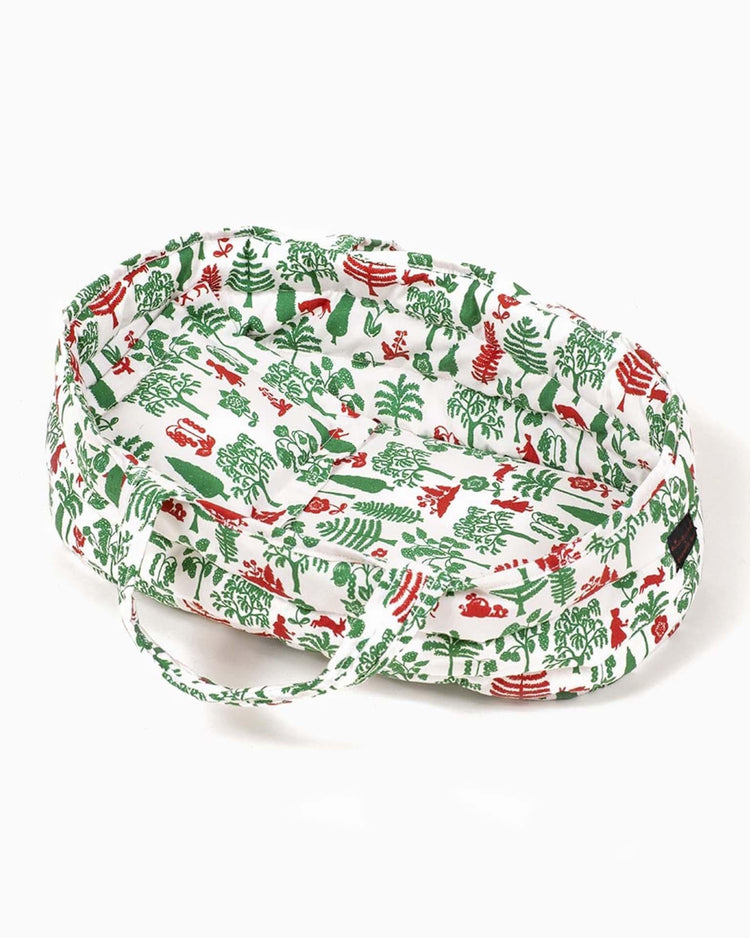The Nathalie Lété bassinet + pillow in trees & chaperon by minikane is a charming small oval pet bed with a white background adorned with vibrant red and green forest-themed designs of trees, animals, and plants, making it perfect for Minikane dolls or Paola Reina collections.