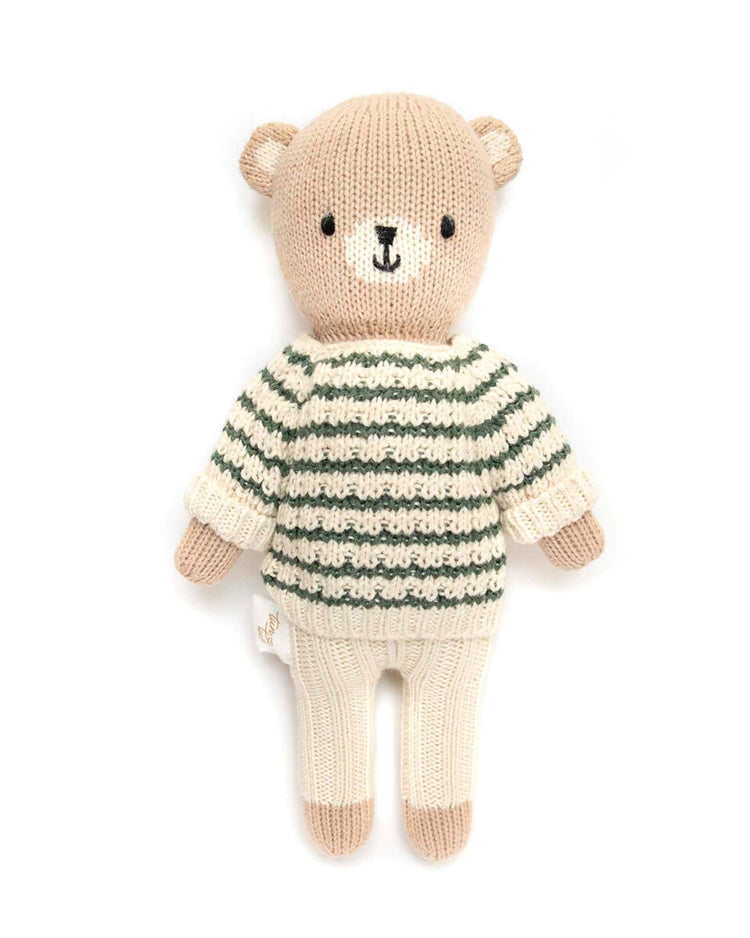 A knitted teddy bear from tun tun, made with Peruvian Pima cotton, is dressed in a natural and green striped sweater paired with cream pants.