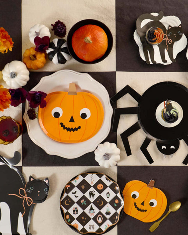 A Halloween-themed table setting with pumpkin, cat, and spider plates, small pumpkins, and festive Halloween party decorations on a black and white checkered tablecloth—perfectly accented by playful meri meri halloween pumpkin napkins for a spirited touch.
