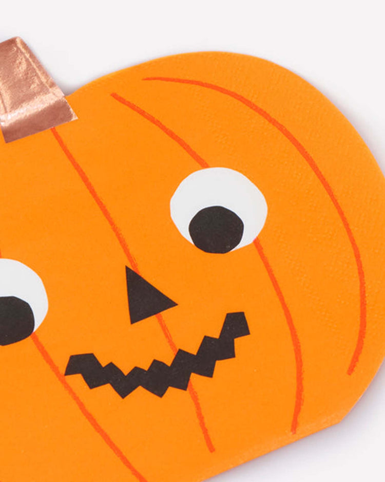 A close-up of the halloween pumpkin napkins by meri meri, featuring a playful pumpkin illustration with googly eyes, a triangle nose, a zigzag mouth, an orange body accented with red lines, and a shiny copper-colored stem—perfect for adding festive charm to your Halloween party decorations.