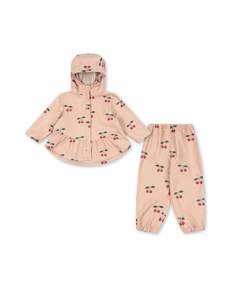 Introducing the *faire rain set in ma grande cerise blush* by konges sløjd—a charming two-piece toddler outfit in light pink, adorned with playful cherry prints. This lightweight ensemble features a wind-resistant, hooded jacket with a peplum hem and secure snap buttons, paired with matching elastic-waist pants for a comfortable and stylish fit.