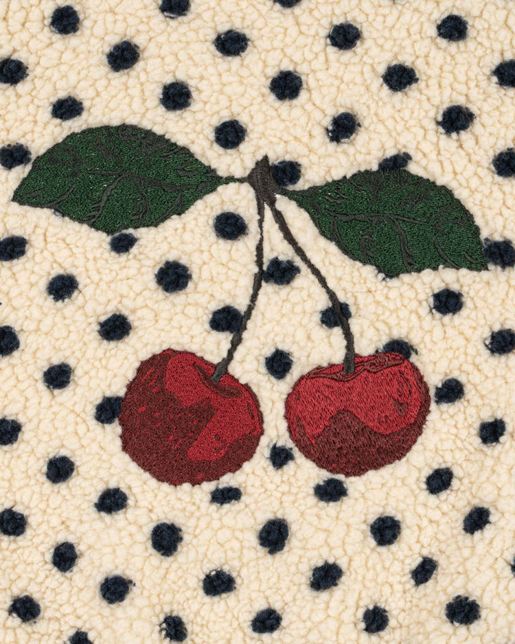 Two red cherries with green leaves are embroidered on cream-colored, textured dot lumiere fabric with a pattern of black polka dots, crafted from luxurious OEKO-TEX certified materials for added peace of mind. This is the jody embroidery teddy jacket by konges sløjd.