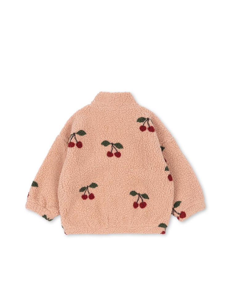 The jody teddy jacket in ma grande cerise blush by konges sløjd is a light pink, fuzzy transitional kids’ jacket made from recycled polyester pile fleece. It features a repeated cherry pattern with green leaves and is shown from the back against a white background.