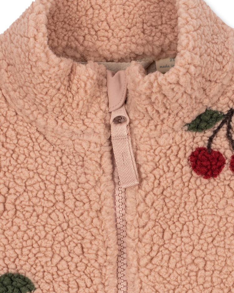 Close-up of the konges sløjd jody teddy jacket in ma grande cerise blush—a pink pile fleece kids transitional jacket, crafted from recycled polyester, featuring a zipper and embroidered red cherries with green leaves near the collar.