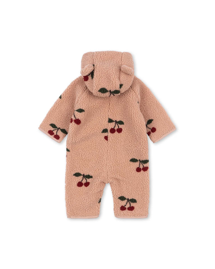 Introducing the konges sløjd Jody Teddy Onesie in Ma Grande Cerise Blush: a cozy, light brown hooded onesie crafted from soft recycled polyester fleece, adorned with playful red cherry patterns and finished with adorable bear ears on the hood. The onesie is presented flat to showcase its back view.
