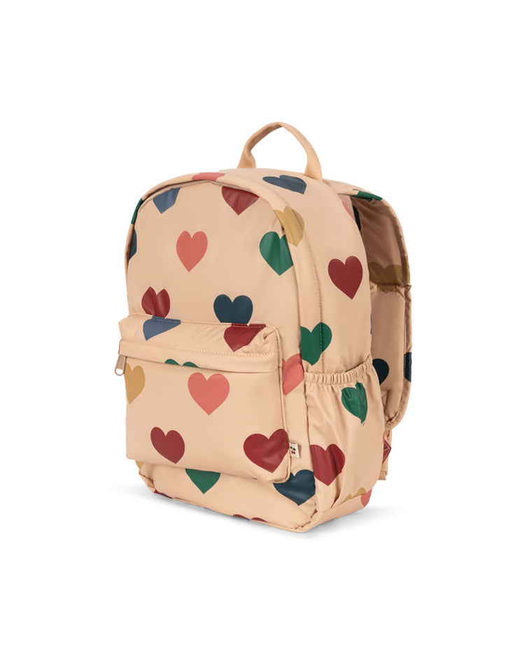 The rainy backpack in bon coeur coloré by konges sløjd is a lightweight kids adventure backpack adorned with a playful pattern of red, green, blue, and yellow hearts. It features a convenient front pocket and side pouch, and is showcased against a white background.