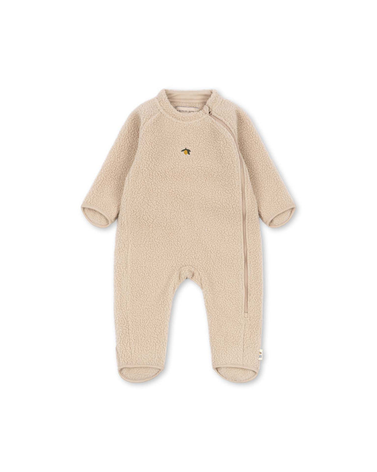 The safa onesie in oxford tan by konges sløjd is a beige baby fleece onesie featuring long sleeves, covered feet, and an asymmetrical front zipper. A small yellow bee is embroidered on the chest. Made from soft, OEKO-TEX certified recycled polyester, the onesie is shown laid flat on a white background.