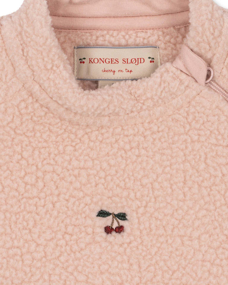 Close-up of the safa onesie in rose smoke by konges sløjd, crafted from recycled polyester fleece. This charming pink baby onesie features a small embroidered cherry detail, a sewn-in "Konges Sløjd cherry on top" label inside the collar, and foldable cuffs for extra comfort and practicality.
