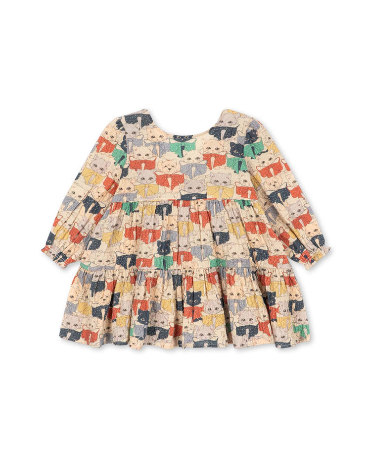 The konges sløjd elin long sleeve bow dress in like cats and dogs features voluminous, ruffled long sleeves and a playful all-over print of colorful illustrated cat faces on a cream background, making it perfect for children.