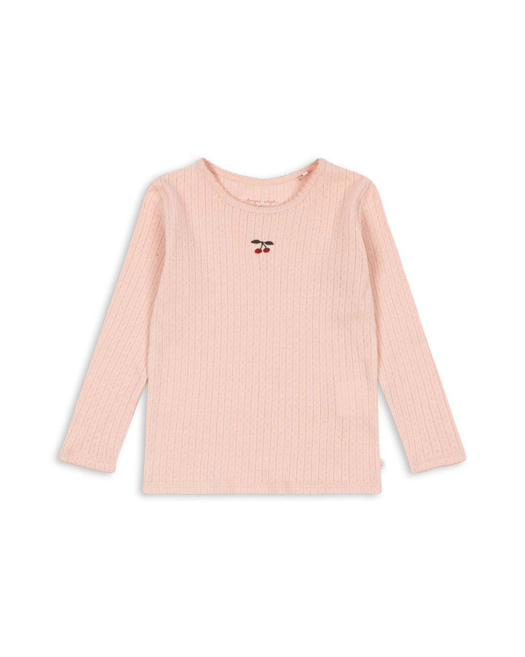 The "minnie blouse in pale blush" by konges sløjd is a light pink, long-sleeve ribbed shirt crafted from soft organic cotton, featuring a small embroidered cherry design on the chest—perfect as a gentle baby base layer and shown on a white background.
