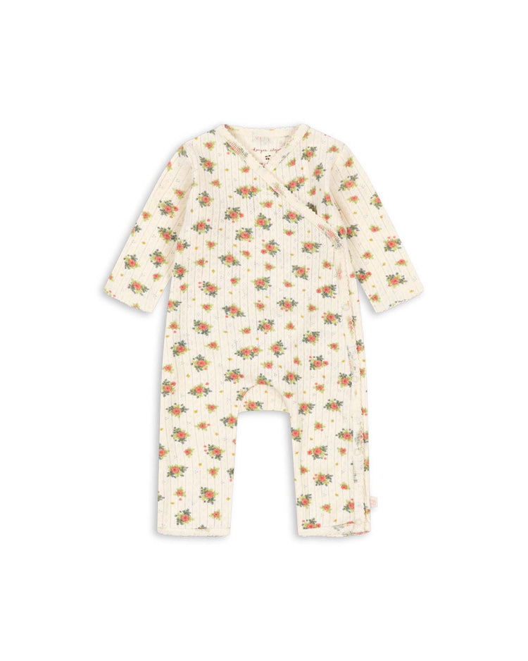The minnie newborn onesie in rosetto by konges sløjd is a cream-colored, long-sleeve baby romper with a wrap front and snap closures. Crafted from soft, GOTS certified organic cotton, it features a ribbed texture and is adorned with an all-over pattern of small orange floral prints.